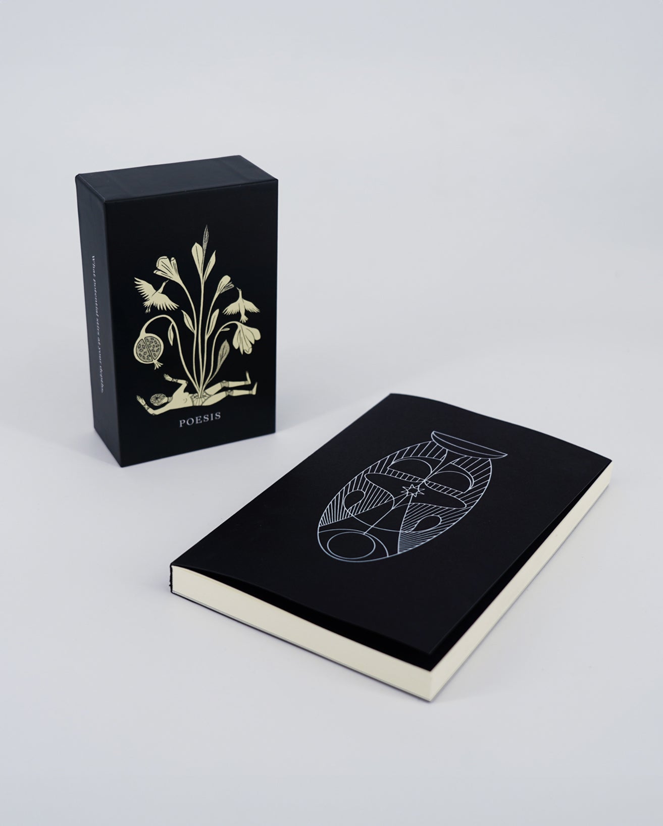 A set of Poesis Oracle Deck and Guide Book. The deck is inside a black box with gold designs, and the guide book is placed beside it with visible white and gold foil deboss on the cover.