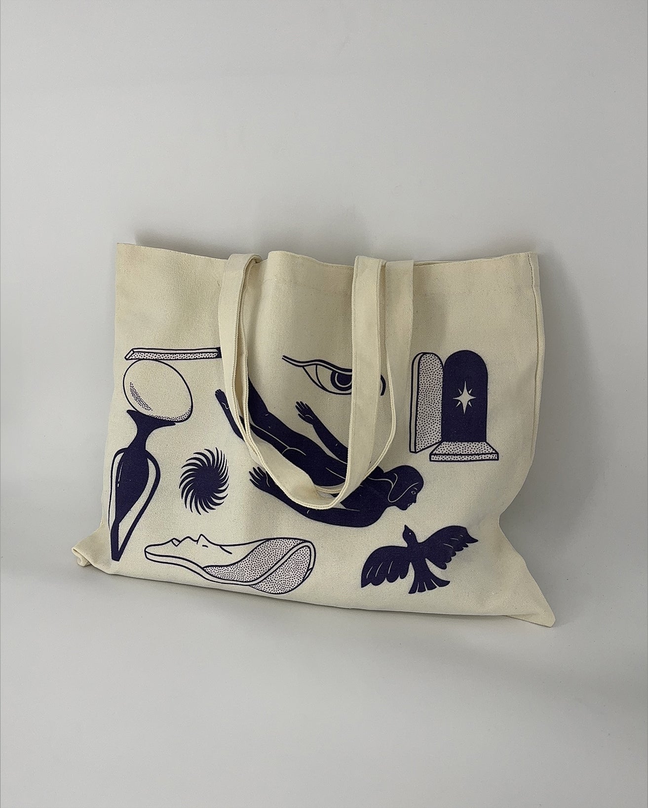 A canvas tote bag with a printed design featuring a diver, a soaring bird, a swirling star, an eye, a match, and an egg.