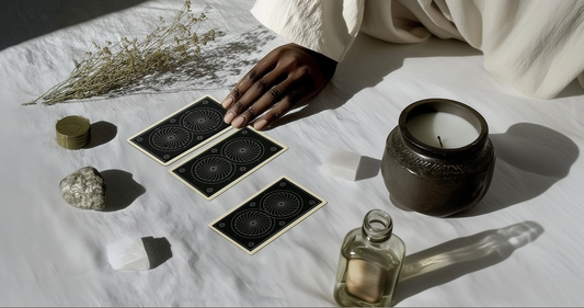 A hand hovers gently over three oracle cards laid on a sunlit cloth, surrounded by ritual objects—crystals, a candle, dried flowers, and sacred tokens—inviting stillness, intuition, and inner inquiry.