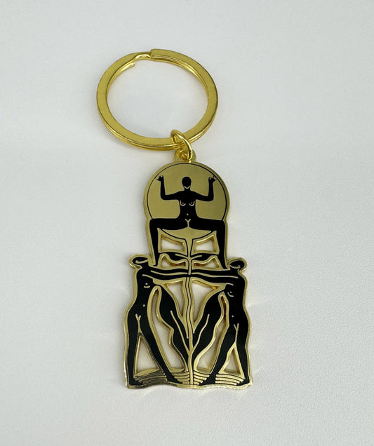 A golden keychain with a hard enamel design featuring a stylized, black-outlined figure. The keychain has a four-link chain and a keyring.
